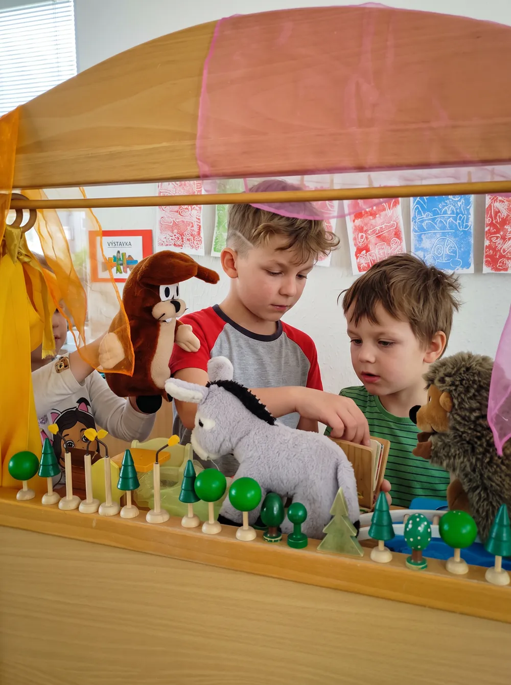 Děti si hrají s maňásky v dřevěném loutkovém divadle ve třídě
