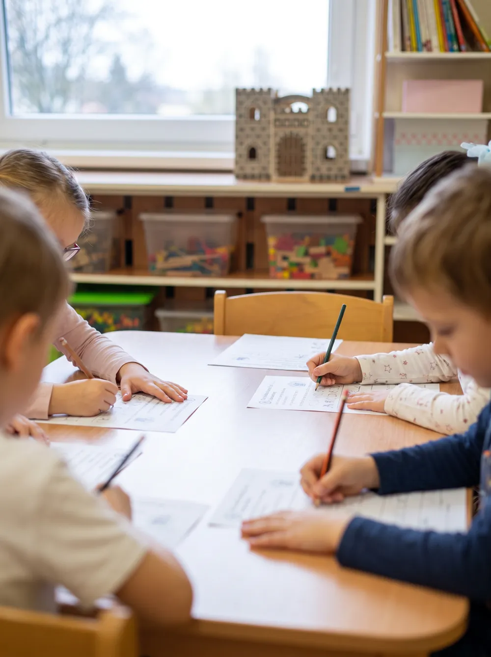 Děti u stolu vyplňují pracovní listy tužkami
