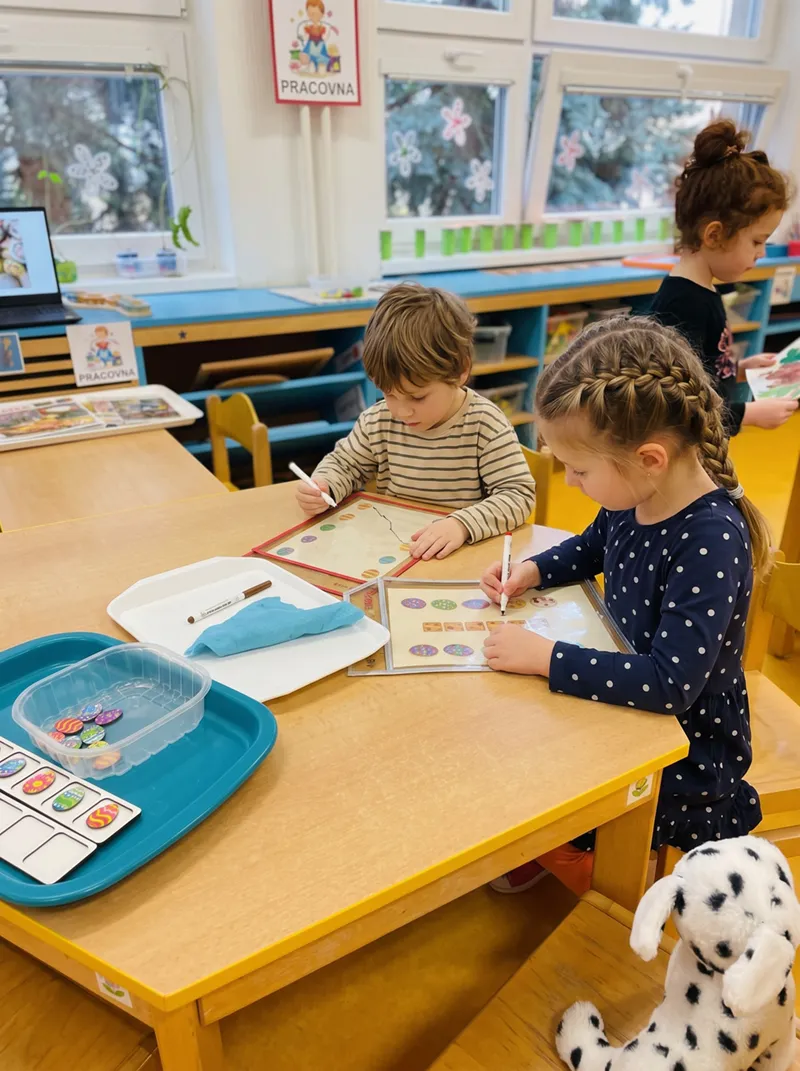 Dvě děti u stolu kreslí fixami do pracovních listů