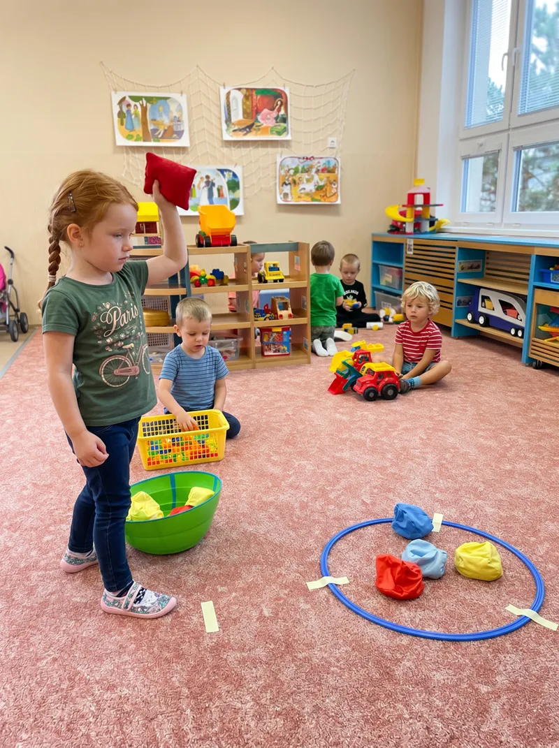Děti si ve třídě hrají s obručí a barevnými pytlíky